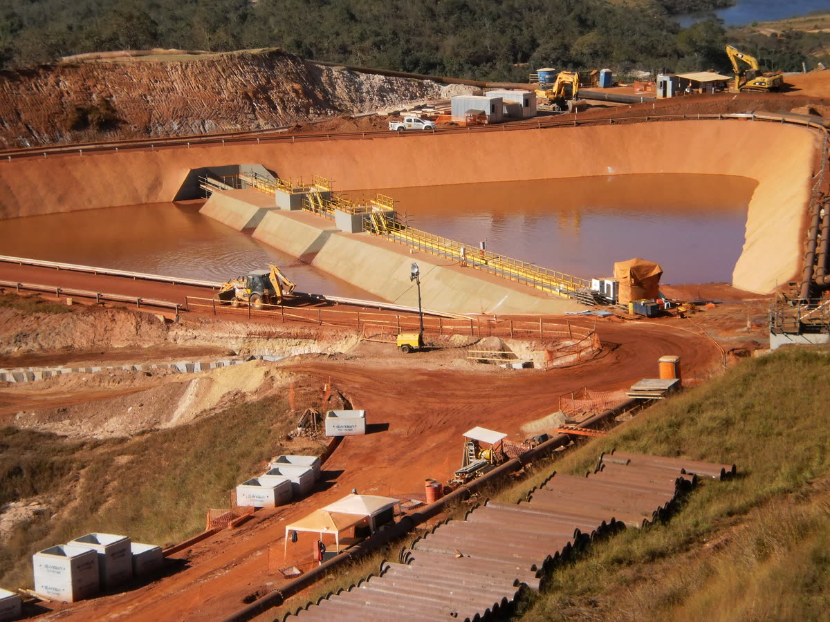 Vista aérea da obra de contenção de rejeito, com bacia, taludes e equipamentos em operação