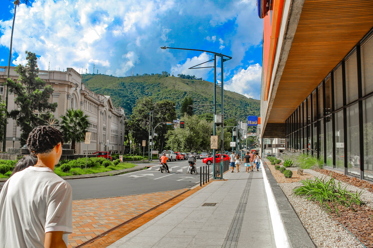 Calçada revitalizada em avenida do centro da cidade, com piso podotátil, canteiros novos e a serra ao fundo