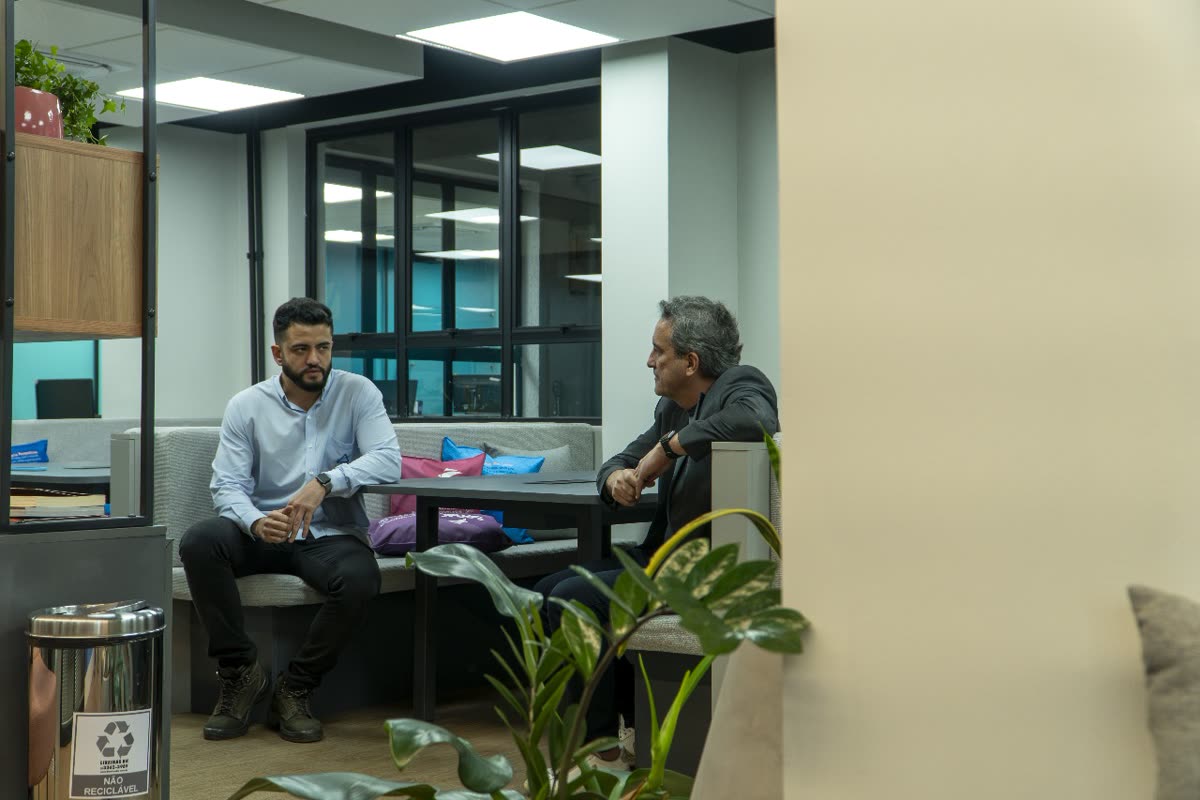 Espaço colaborativo entregue após retrofit, com divisórias de vidro em perfil metálico preto, marcenaria e área de estar