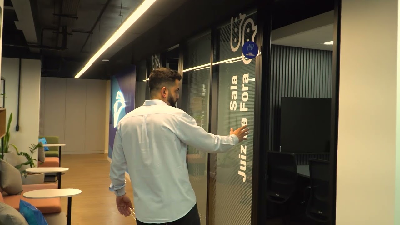 Corredor de escritório corporativo entregue, com salas de reunião envidraçadas, iluminação linear no teto e área de lounge